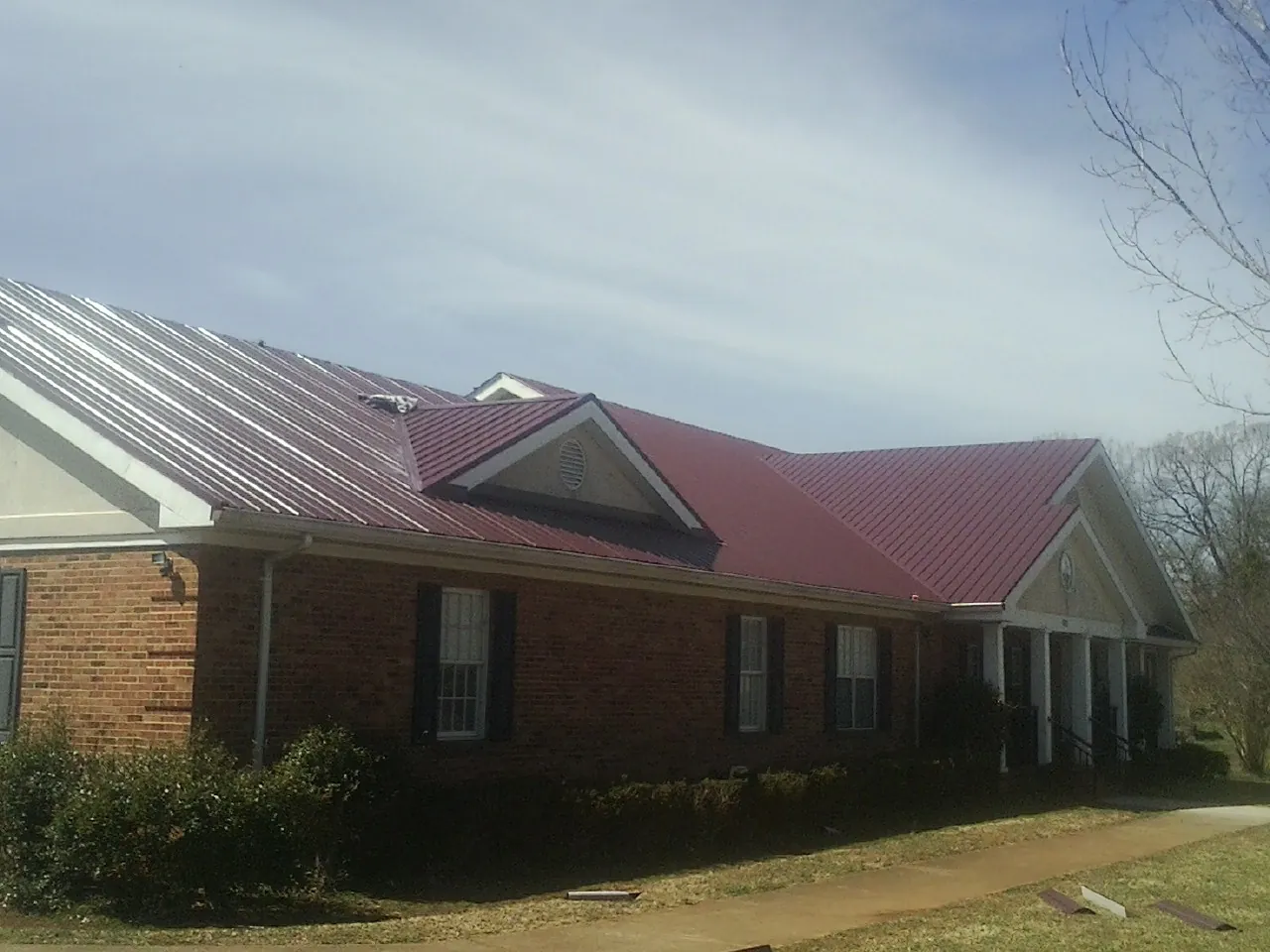 Red metal roof with gabled entries on a long brick building, from a Hail Damage Roof Repair job in North Billerica