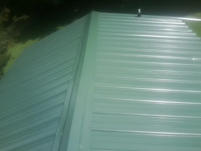 New green metal panels meeting at the ridge of a roof — Flat Roof Repair work by our crew in North Billerica