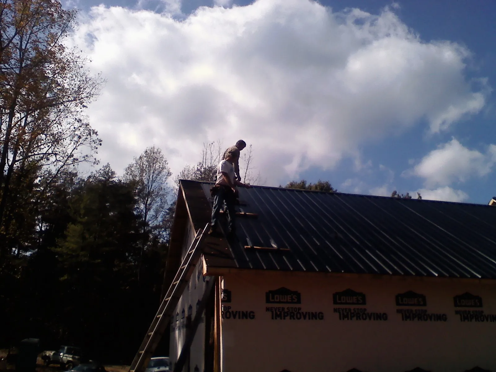 Roofer fastening dark metal panels high against a cloudy sky, from a Roof Inspection job in North Billerica