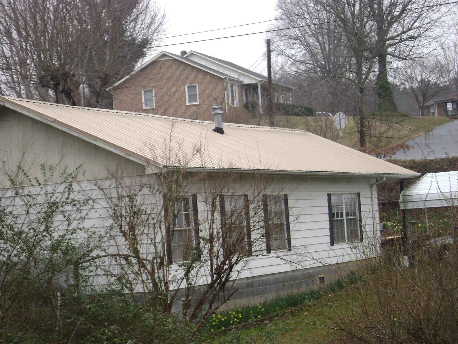 Tan metal roof on a white sided house set into a hillside — Commercial Roofing by Roofing Brothers in North Billerica